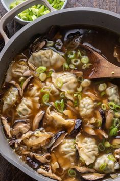 a pot filled with dumplings and vegetables on top of a wooden table next to other dishes