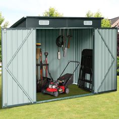 a green shed with tools in it and lawn mowers on the grass next to it