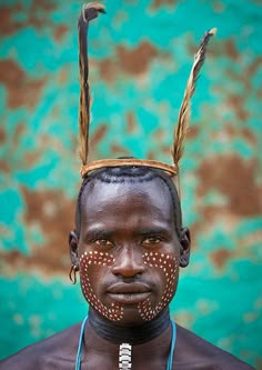 an african man with feathers on his head and nose piercings in front of a turquoise background