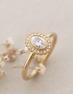 a gold ring with a white diamond in the center and flowers around it on a table