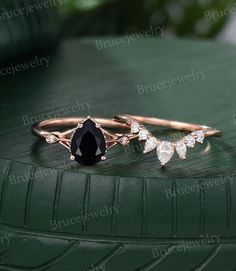 two gold rings with black and white diamonds on them sitting on top of a green leaf