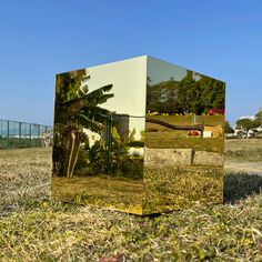 a mirrored cube sitting on top of a grass covered field