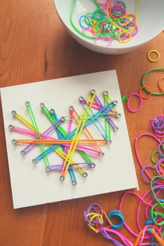 there are lots of colored paper clips on the table next to a bowl with scissors