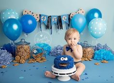 a baby sitting in front of a cookie monster cake surrounded by blue balloons and streamers