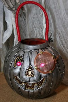 a metal pumpkin shaped container with a face on it's side and red handles