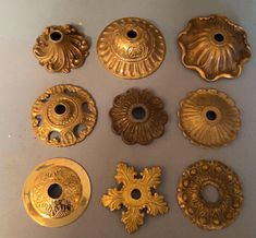 nine brass knobs and covers on a white surface with holes in the middle one has an ornate design