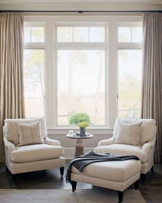 a living room with two white chairs and a coffee table in front of a large window