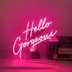 a pink neon sign that says hello gorgeous on top of a bed next to some books