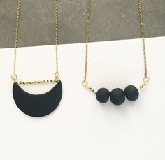 two necklaces with black beads hanging from gold chains on a white surface, next to each other