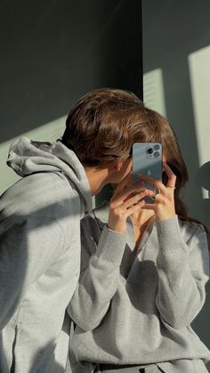 a woman taking a selfie with her cell phone in front of her face and wearing a gray sweater