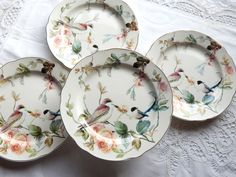 four plates with birds on them sitting on a white tablecloth covered table next to a lace doily