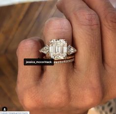 a woman's hand holding a ring with an emerald and diamond set in it