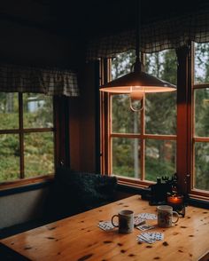 two coffee mugs on a wooden table in front of large windows with forest outside