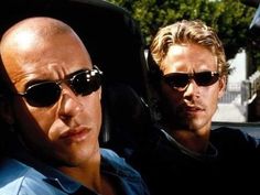 two men sitting in the back seat of a car, one with sunglasses on his head