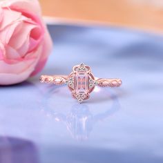 a pink rose sitting on top of a table next to an engagement ring with diamonds