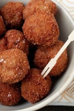 a white bowl filled with fried food on top of a wooden table next to utensils