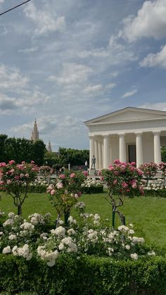 a white building with columns and flowers in the foreground, surrounded by greenery