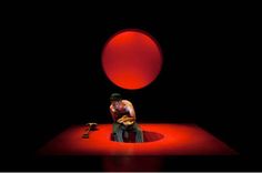 a man sitting on top of a red floor next to a black background with an orange ball