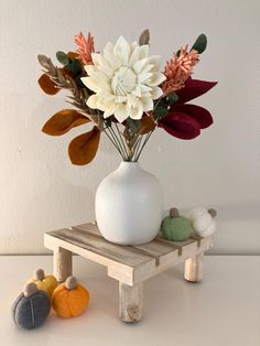 a white vase filled with flowers sitting on top of a wooden table next to small pumpkins