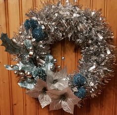 a wreath with silver and blue decorations hanging on a wooden wall next to a door