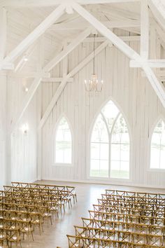 an empty church with rows of chairs and chandeliers on the ceiling, in front of two large windows