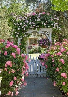 a white bench surrounded by pink flowers and greenery in front of a garden gate