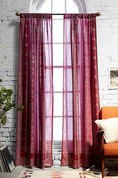 a living room with a chair and window covered in red sheer curtaines on the windowsill