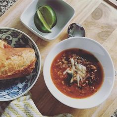 two bowls of chili soup with bread and an avocado slice on the side