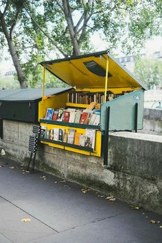 a yellow book stand sitting on the side of a road next to a tree filled street