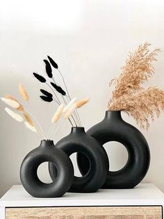 two black vases sitting on top of a white shelf next to dried plants and dry grass