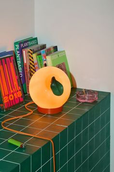 an orange lamp sitting on top of a green table next to books and other items