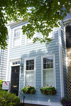 a blue house with white trim and three flower boxes on the front window sill