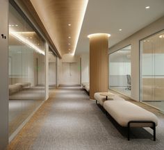 a long hallway with benches and glass walls on both sides is lit by recessed lights