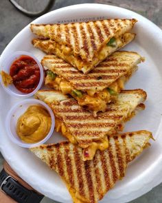 a white plate topped with grilled sandwiches and dipping sauces on top of it