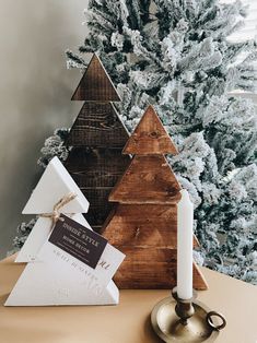 three wooden christmas trees sitting on top of a table next to a candle and some decorations