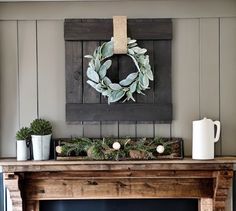 a mantel with a wreath on top of it and two mugs next to it