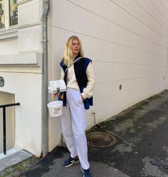 a woman standing in front of a white building holding a bucket and wearing sweatpants