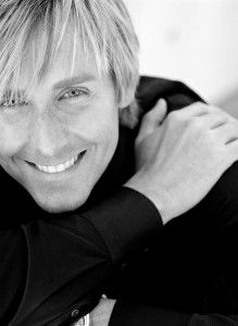 a man with blonde hair is smiling and holding his arms around his neck while wearing a black shirt