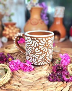 a coffee cup sitting on top of a wicker table next to some purple flowers