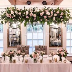 the table is set up with flowers and greenery for an elegant wedding reception in front of large windows