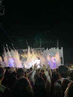 a large group of people at a concert with their hands in the air as fireworks go off