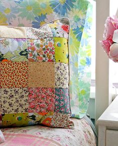 a colorful patchwork pillow sitting on top of a bed next to a vase with flowers