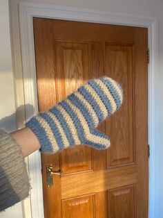 a person is holding up a knitted mitt in front of a wooden door