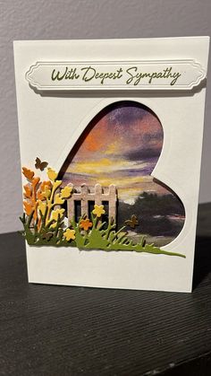 a greeting card with an image of a gate and flowers in the grass, on top of a wooden table