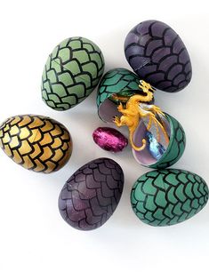 an assortment of painted eggs with dragon figurines in them on a white surface