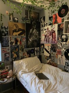 an unmade bed in a room with posters on the wall and plants hanging from the ceiling