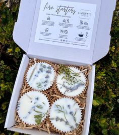 four cupcakes with white frosting and blue flowers in a box on some grass