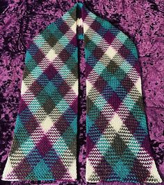 two knitted scarves sitting on top of a purple velvet floor covered in green and white checkered fabric