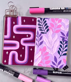 an open notebook with pink and purple designs next to markers, pencils and marker pens