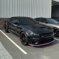 two cars parked next to each other in front of a metal building with pink trim